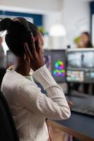 Black editor working with footage on pc with two monitors, putting on headphones. African videographer editing movie using post production software working in creative start up agency office. photo