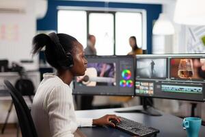 Black woman editor developing new project film montage sitting in modern creative agency office. Content creator in digital multimedia company processing movie with post production software photo