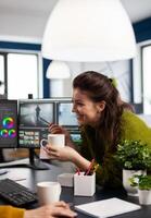 Happy videographer editing project drinking coffee using post production software working in digital multimedia company with dual monitors setup. Retoucher processing audio film montage on pc photo