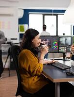 Enjoyed woman videographer editing project drinking coffee using post production software working in digital multimedia company with two monitors. Retoucher processing audio film montage on pc photo
