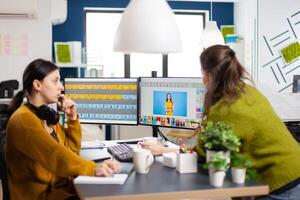 Confident women photo editors sitting at workplace in creative studio retouching photo, art director explaning color greding technic. Retouchers editing with drawing tablet and stylus pencil