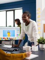 Satisfied african photo editor discussing with colleague how retouching image, working on PC. Woman retoucher editing assets in pro software app with graphic tablet sitting in creative agency