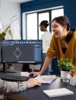 Excited mechanical engineers laughing and discussing about manufacturing new project, taking break. Man technician working at pc, screen shows 3D engine made with CAD software, using computer photo