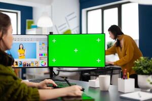 Creative woman retoucher editing assets in digital retouching program, working concentrated in photo production studio looking in computer with green screen, chroma key mockup isolated display.