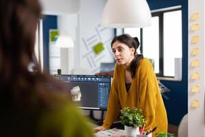 Woman industrial designer discussing with colleague standing at desk while working in CAD program, designing 3D prototype of components. Engineer sharing ideas for construction mechanism photo