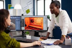 Multiethnic women game designer looking at computer with dual displays working together at project in studio office. Gamer workers developing new online games on pc with modern technology photo