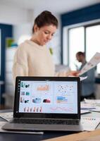 Laptop with financial charts on office of start up company. Executive entrepreneur, manager leader standing working on projects with diverse colleagues. Successful corporate professional entrepreneur online internet statistics photo