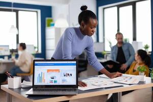African entrepreneur of start up company reading charts on documents paperwork. Diverse team of business people analyzing company financial reports from computer. Successful corporate professional entrepreneur online internet statistics photo