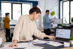Busy businesswoman employee concentrated on company charts scrolling on laptop. Successful corporate professional entrepreneur online internet statistics. Executive entrepreneur, manager leader standing working on projects with diverse colleagues. photo