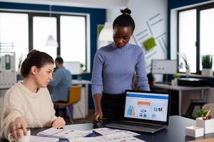 Diverse businesswomen discussing new project for company evolution, black woman checking tasks on new contract. Multiethnic employees gathered in co-working space. photo