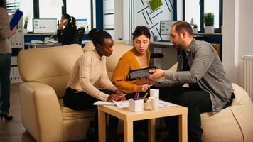 Multiethnic team analysing informations from tablet discussing sitting on couch brainstorming on new project for start up company. Diverse businesspeople analysing financial reports during meeting. photo