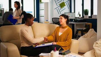 Pleased multiracial business partners sitting on couch in modern office shaking hands after signing partnership contract. Diverse team being happy for successful negotiations in start up company. photo