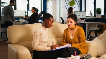 Young diverse woman holding paper document, discussing contract with confident partner in casual wear, signing investment papers. Businesswomen shaking hands, making satisfactorily agreement. photo