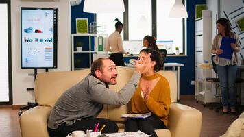 Angry man manager arguing woman employee for bad work result, sitting on couch, while diverse colleagues working scared in background. Business woman employee raging about multitasking difficult job. photo
