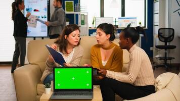 International business team talking to african woman discussing company plan with mockup laptop in front of camera. Leader explainig project strategy using green screen pc with chroma key display. photo