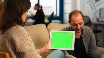 Business people sitting on couch analysing financial statistics, holding tablet with green screen while diverse team working on background. Multiethnic coworkers planning project on chroma key display photo