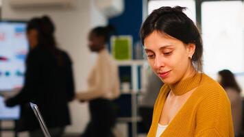Young woman in casual clothing working at laptop sitting at desk in busy financial startup company while diverse team analyzes statistics data in modern office. Multiethnic team concentrated on work photo