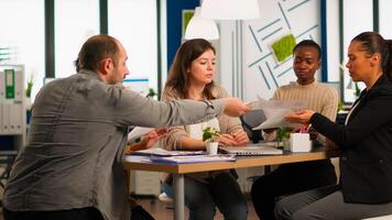 Young diverse team of workers talking, looking at documents and analyzing graphs data sitting at workplace desk in start up company. Professional colleagues team discussing marketing project. photo