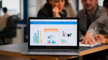 Laptop screen ready for financial project presentation placed on desk while business people work in background. Diverse employees gathered in co-working, working process in busy company, teamwork help photo