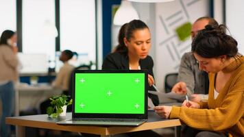Laptop with green screen ready for presentation placed on desk while business people work in background. Group of employees using notebook with chroma key display. mock up monitor photo