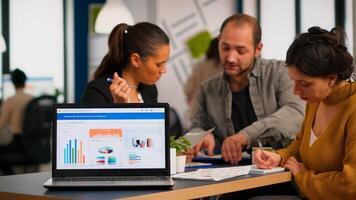 Business woman talking about financial project, taking notes, discussing start up ideas using laptop. Diverse employees gathered in co-working, working process in busy company, teamwork help concept photo