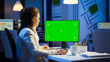 Woman looking at computer with chroma key during night time in start up business office working overtime. Freelancer watching desktop monitor mockup display with green screen, typing writting photo