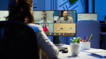 Back view of business woman talking about sale report in conference working overtime in start-up office. Team using online wireless communication discussing on webcam during group meeting. photo