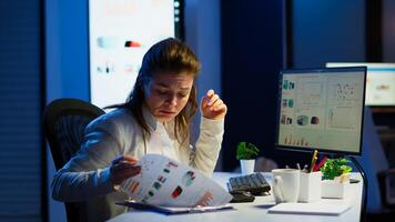 Tired freelancer comparing graphics from clipboard and computer working from business office overtime. Busy focused employee using modern technology network wireless reading typing, searching photo