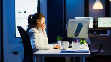 Tired designer engineer analizing new prototype of 3D model of the plant yawning working overtime. Industrial female worker studying turbine idea on pc showing cad software on device display photo