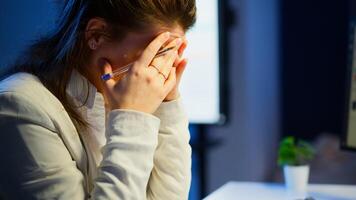 Close up of stressed busy woman with headache working from business office late at night. Tired focused employee using modern technology network wireless doing overtime for job checking reports photo