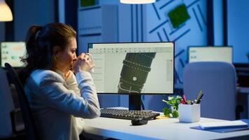Woman engineer working late at night on a 3D model of industrial turbine drinking coffee in front of computer. Remote freelancer studying prototype idea on pc showing cad software on device display photo