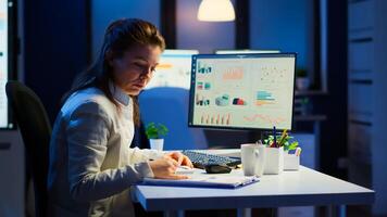 Exhausted manager trying to finish business project respecting deadline working at night in front of computer taking notes writing on notebook. Tired employee overtime sitting at desk in workplace photo