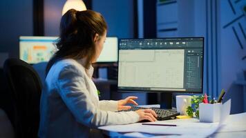 Woman architect matching digital plans from pc with blueprints working in start-up business office overtime. Designer using cad software to design a 3D concept of buildings creating late at night photo