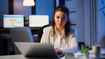 Tired woman manager raising head looking at camera sighing after typing on laptop, working late at night in start-up business office. Focused employee using technology network wireless doing overtime photo