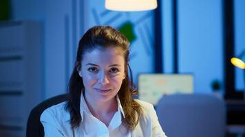 Close up portrait of business woman smiling at camera after reading mails on laptop sitting at desk in start-up company late at night. Focused employee using technology network wireless doing overtime photo