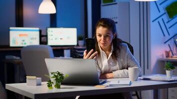 Business woman discussing during conference with partners using smartphone and headphone late at night working in start-up office. Employee with modern technology network wireless doing overtime photo