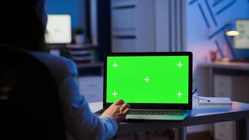 Woman looking at laptop with green mockup during night time in start up business office working overtime. Freelancer watching desktop monitor display with green screen, chroma key, typing writting photo