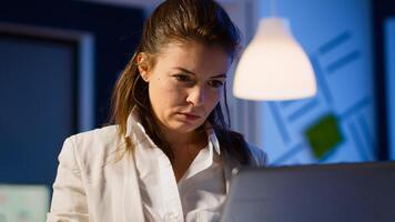 Close up of concentrated entrepreneur analysing financial reports standing in start up office late night holding laptop. Focused employee using technology network wireless overtime reading, searching photo