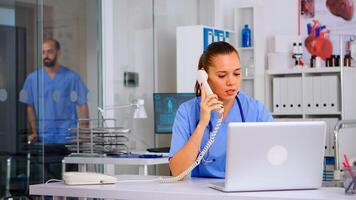 Medical staff talking with patient on phone from hospital about diagnosis, male nurse working in background. Healthcare physician, receptionist doctor assistant helping with telehealth communication photo