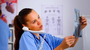 Close up of assistant answering phone checking the result of patient x-ray and diagnosing him. Healthcare physician in medicine uniform, receptionist doctor nurse helping with telephone concultation photo