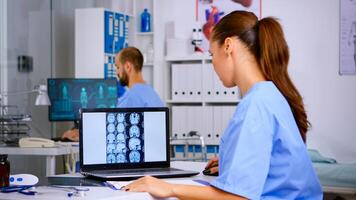 Doctor assistant analyzing skull brain x-ray tommography medical data on laptop, taking notes on clipboard. Radiologist in medicine uniform looking at digital radiography, examination, diagnosis. photo