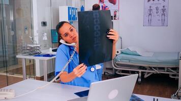 Nurse receptionist answering at hospital call checking the result of patient x-ray and diagnosing him. Healthcare physician in medicine uniform, doctor assistant helping with phone concultation photo