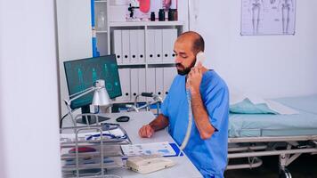 Man healthcare physician answering phone calls working in hospital clinic, helping patient with medical appointment. Receptionist in medicine uniform, doctor assistant during telehealth communication photo