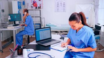 Team of doctors working in hospital clinic, nurse man talking at phone and assistent taking notes. Medical physician in medicine uniform writing list of consulted, diagnosed patients, making research. photo