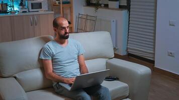 Caucasian male sitting in front of television while working at communication project before deadline on laptop. Tired man browsing on internet using network technology late at night in kitchen photo