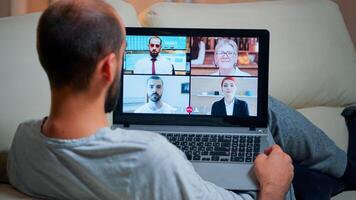 Focused adult using laptop computer during videocall conference talking about social business connection while sitting on couch. Relaxed man working at online communication project overtime in kitchen photo