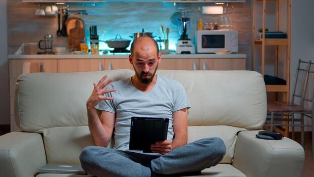 Focused man having online meeting videocall on tablet computer speaking using videoconference online web internet communication. Caucasian man browsing on internet for deadline project photo