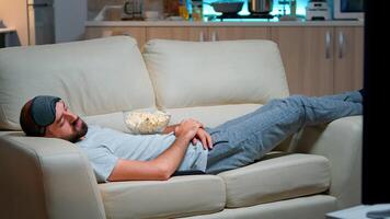 Man closing his eye and falling asleep on the couch in living room in front of the TV, while the television entertainment is ON. Relaxation cinema after a hard week of work photo
