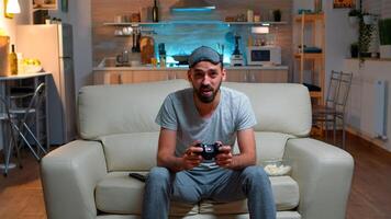 Upset pro gamer sitting in front of television losing soccer games holding wireless controller. Frustrated man with sleep mask lying on sofa late at night in kitchen photo
