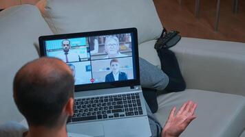 Back shot of tired man lying on sofa while chatting with teammates during business videocall conference use laptop computer. Caucasian male using modern technology wireless late at night in kitchen photo